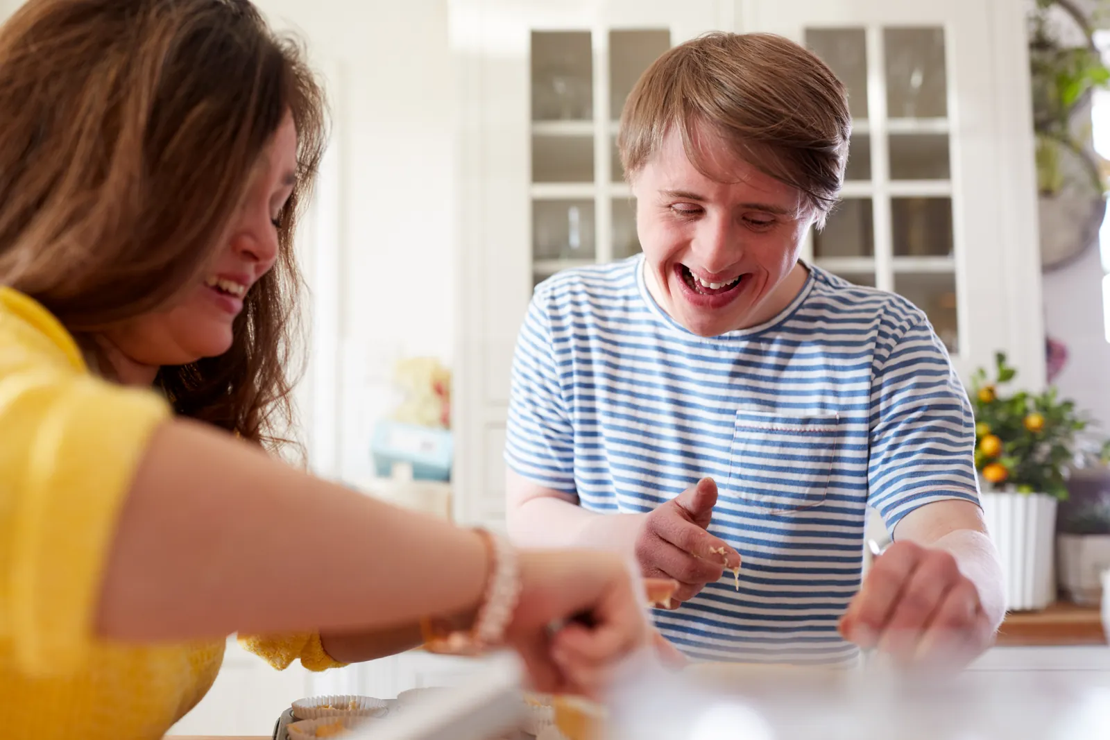 A woman and a young man with intellectual disabilities smile while making cupcakes
