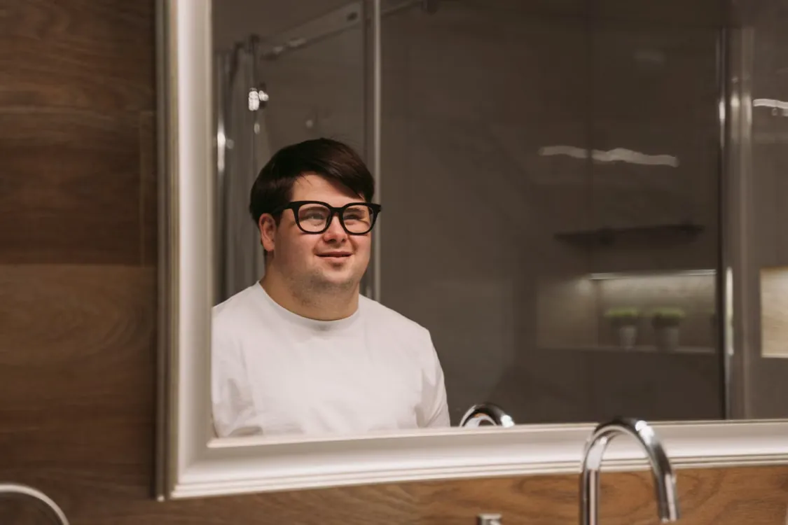 A young man with an intellectual disability smiles while looking in a mirror